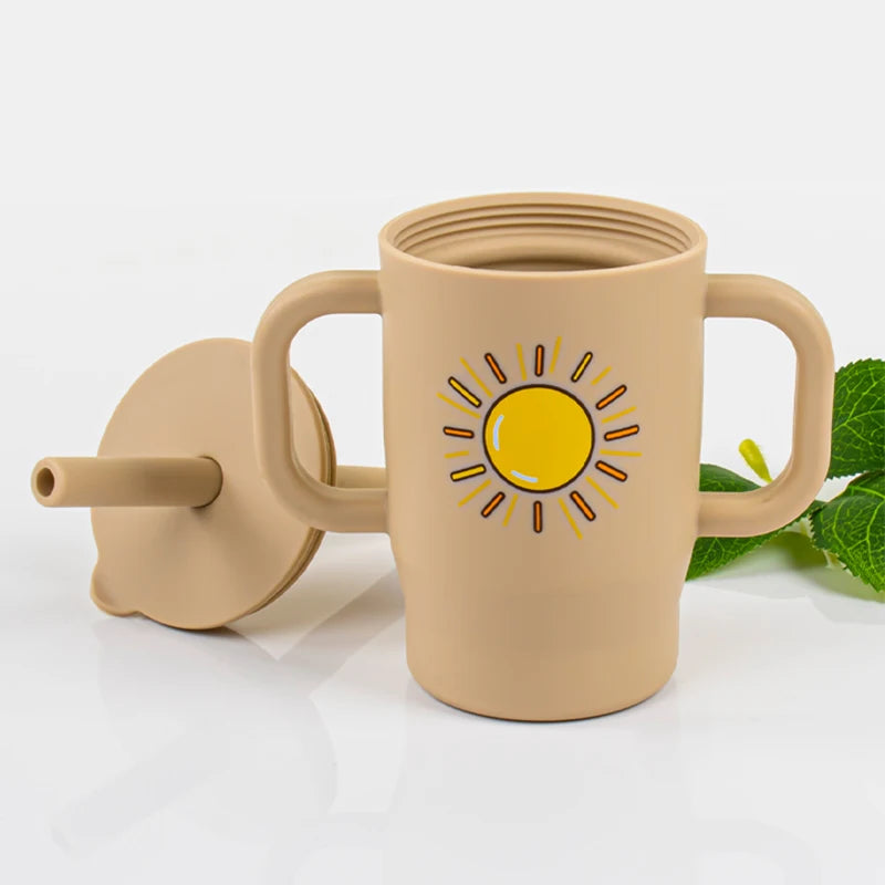 A beige silicone training cup with a straw and handles is shown on a white surface.