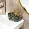 A leaf-shaped ceramic soap dish with a gold drain rack sits on a white bathroom sink.