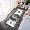 A rectangular banknote pattern anti-slip soft floor mat placed on a gray floor next to a bed.