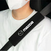 A person wearing a white shirt is holding a black Mazda car seat belt shoulder protector cover.