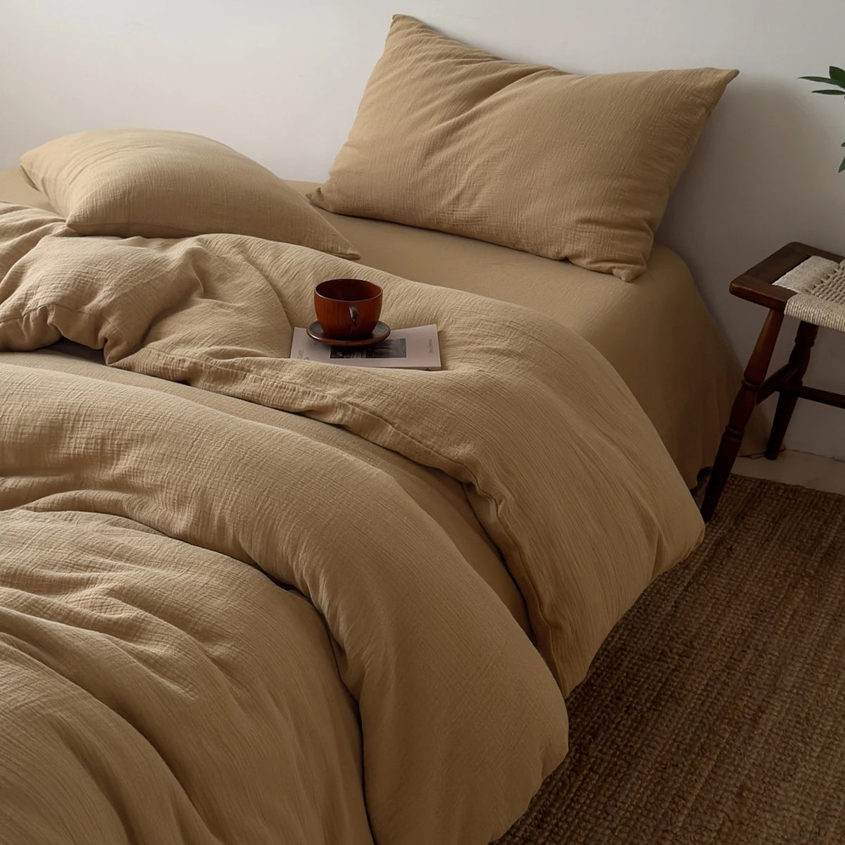 Beige, faltige Bettwäsche mit passender Kissenhülle und einer kleinen braunen Tasse auf einem Bett.