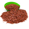 A pile of reddish-brown tumbled crystal stone chips in a green bowl and loose on a white surface.
