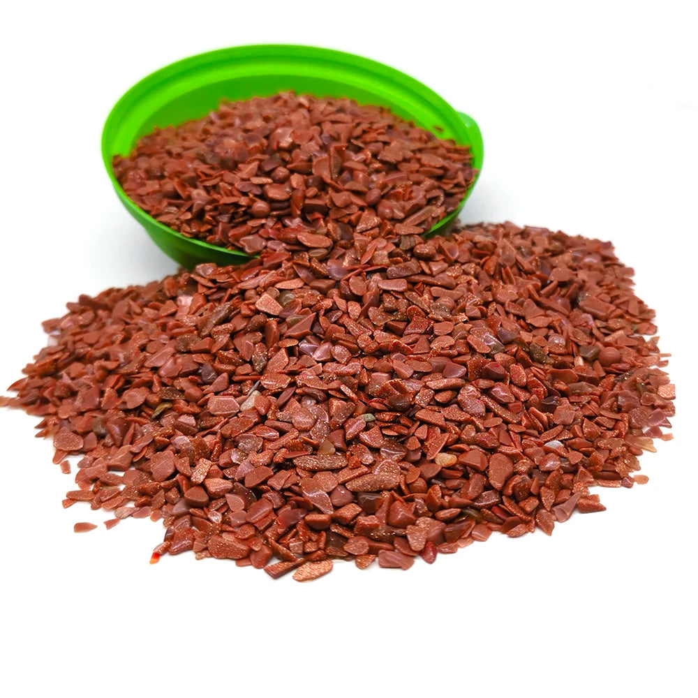 A pile of reddish-brown tumbled crystal stone chips in a green bowl and loose on a white surface.