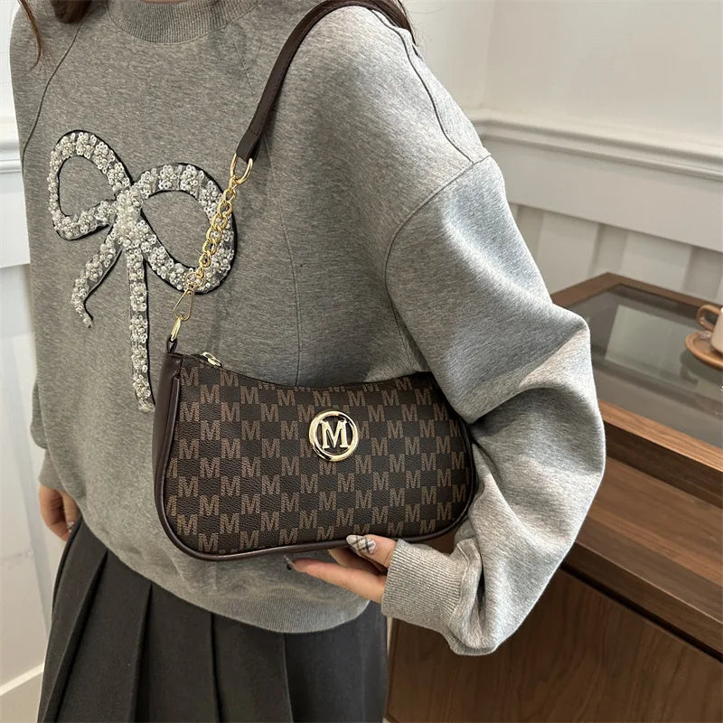 A gray sweatshirt features a vintage-inspired brown leather crossbody bag with a silver 'M' accent charm.