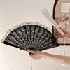 A hand is holding a black lace folding fan with a decorative handle and a white bamboo stick.