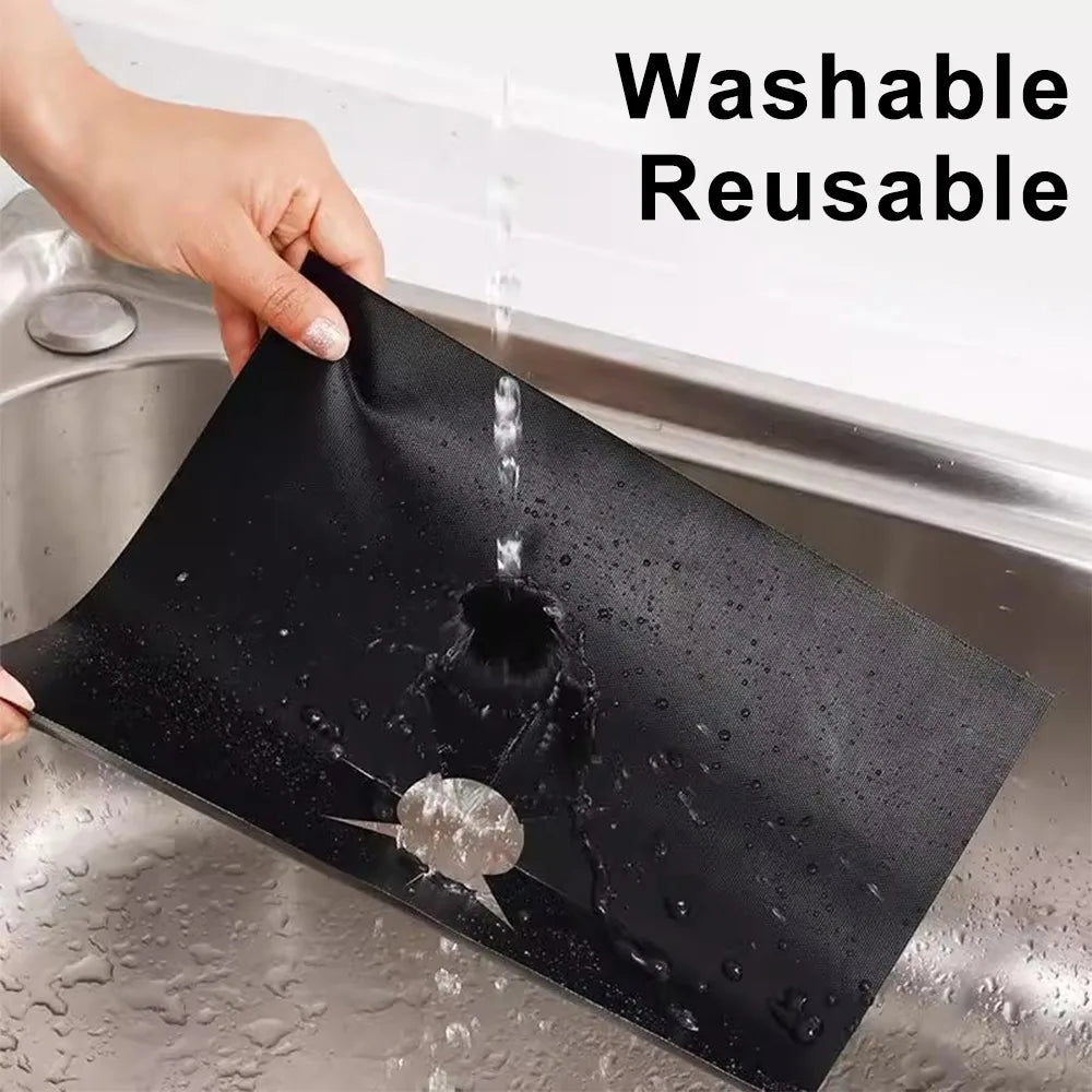 A black square heat-resistant stove burner cover being washed in a kitchen sink.
