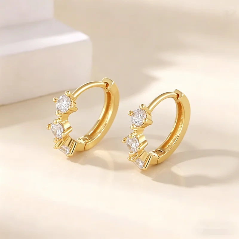 Pendientes de aro dorados con piedras de circonita cúbica, mostrados con luz brillante y suave.