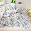 A white quilted blanket with a blue and gray floral pattern is displayed on a shelf with matching pillows.