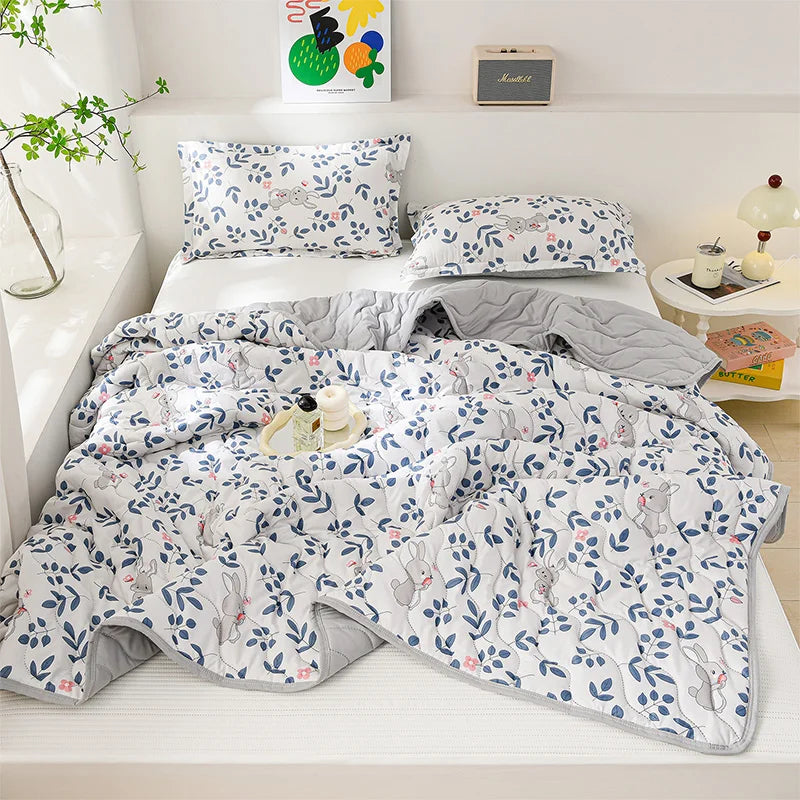 A white quilted blanket with a blue and gray floral pattern is displayed on a shelf with matching pillows.