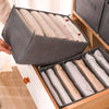 A gray foldable closet organizer box filled with neatly folded white and beige underwear, socks, and accessories.