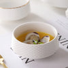 A white ceramic soup bowl filled with a light yellow broth and pieces of meat or seafood.