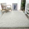 A fluffy white luxury velvet carpet placed on a light wooden floor with a chair and a framed plant artwork.