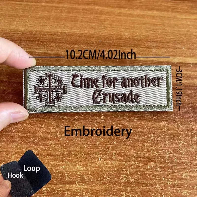 A rectangular embroidered patch with the text Time for another Crusade on a khaki fabric background.