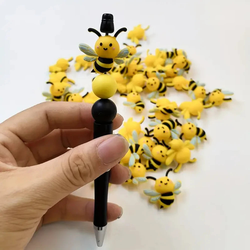 A hand holds a black tool with a yellow bee bead attached, surrounded by many yellow and black silicone bee beads for crafts.