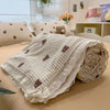 A rolled floral washed cotton gauze summer quilt with small brown embroidered shapes on a tan background.