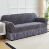 A gray jacquard sofa cover with an elastic skirt is displayed on a light-colored rug in a bright room.