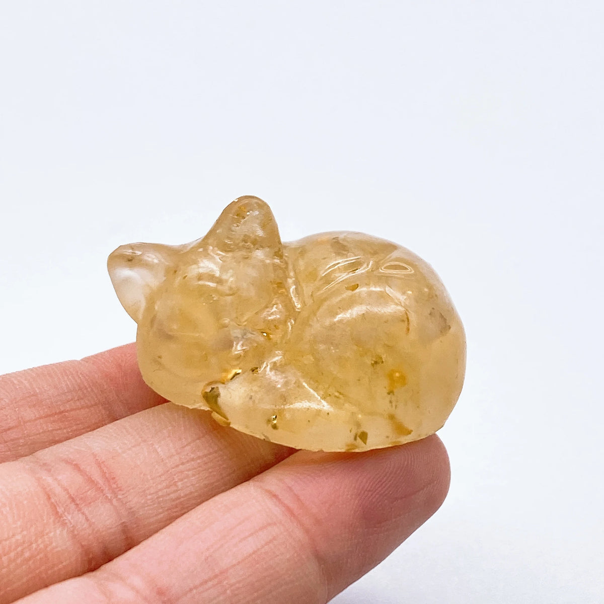A translucent yellow crystal resin figurine shaped like a sleeping cat being held in a hand.