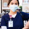 A woman wearing a blue scrubs shirt and a nurse badge reel with an anime design.