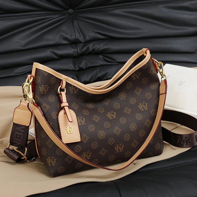 A brown leather tote bag with a monogram pattern and tan strap resting on a dark surface.