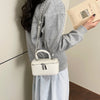 A person holds a cream woven PU leather crossbody bag and a book, against a light wall.