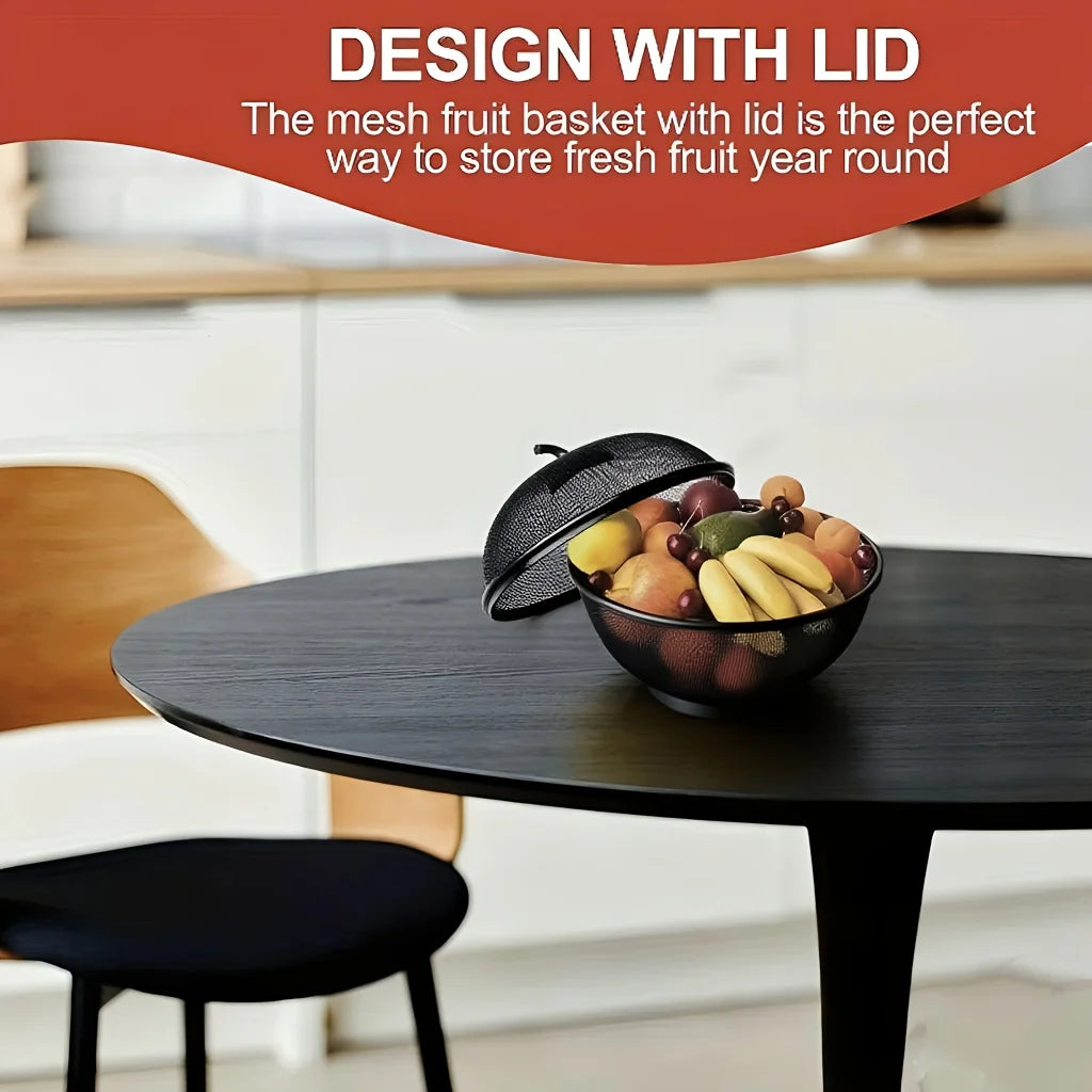 A dark metal fruit basket with a mesh lid filled with fresh fruit placed on a wooden table.
