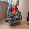An animal print black and white duffle bag with orange straps is held by a person in a light-colored top.
