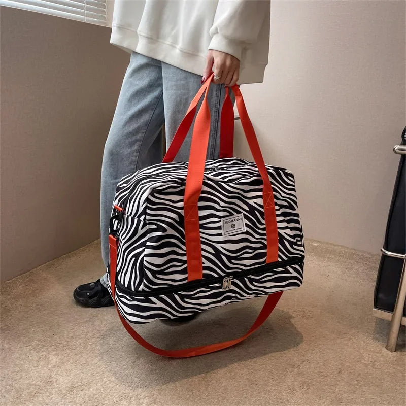 An animal print black and white duffle bag with orange straps is held by a person in a light-colored top.