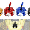 Four colored aluminum motorcycle fuel tank caps with different colored plugs displayed on a yellow motorcycle tank.
