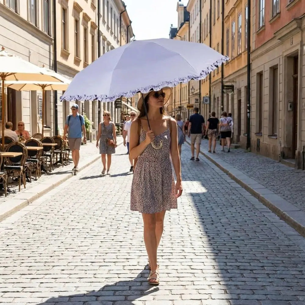 A woman in a patterned dress holds a large white umbrella while walking down a cobblestone street.