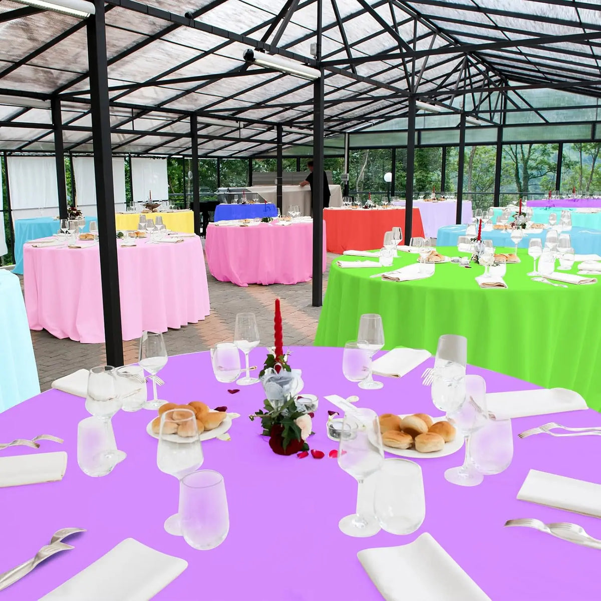 A vibrant purple round tablecloth is set with white plates, silverware, and glassware for an event.