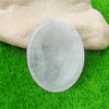 A smooth, oval, translucent crystal stone resting on vibrant green grass next to a hand.