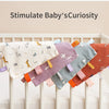 A collection of colorful baby sensory tag comfort blankets with soothing teethers displayed in a crib.
