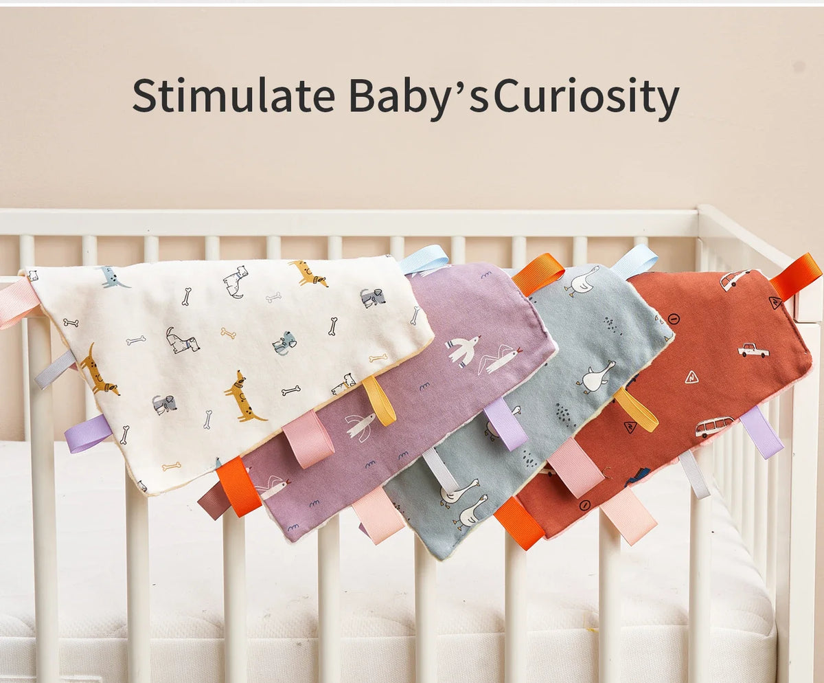A collection of colorful baby sensory tag comfort blankets with soothing teethers displayed in a crib.