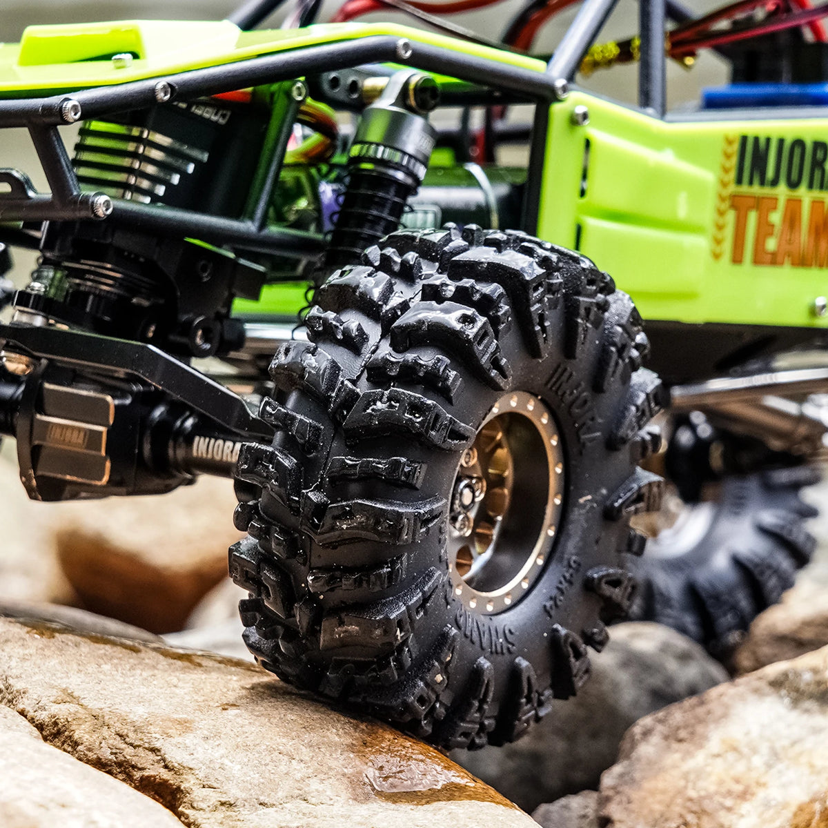 Close-up of a black mud terrain tire mounted on a green RC crawler chassis.