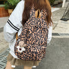 A woman is wearing a leopard print nylon backpack with multiple pockets while standing outdoors.