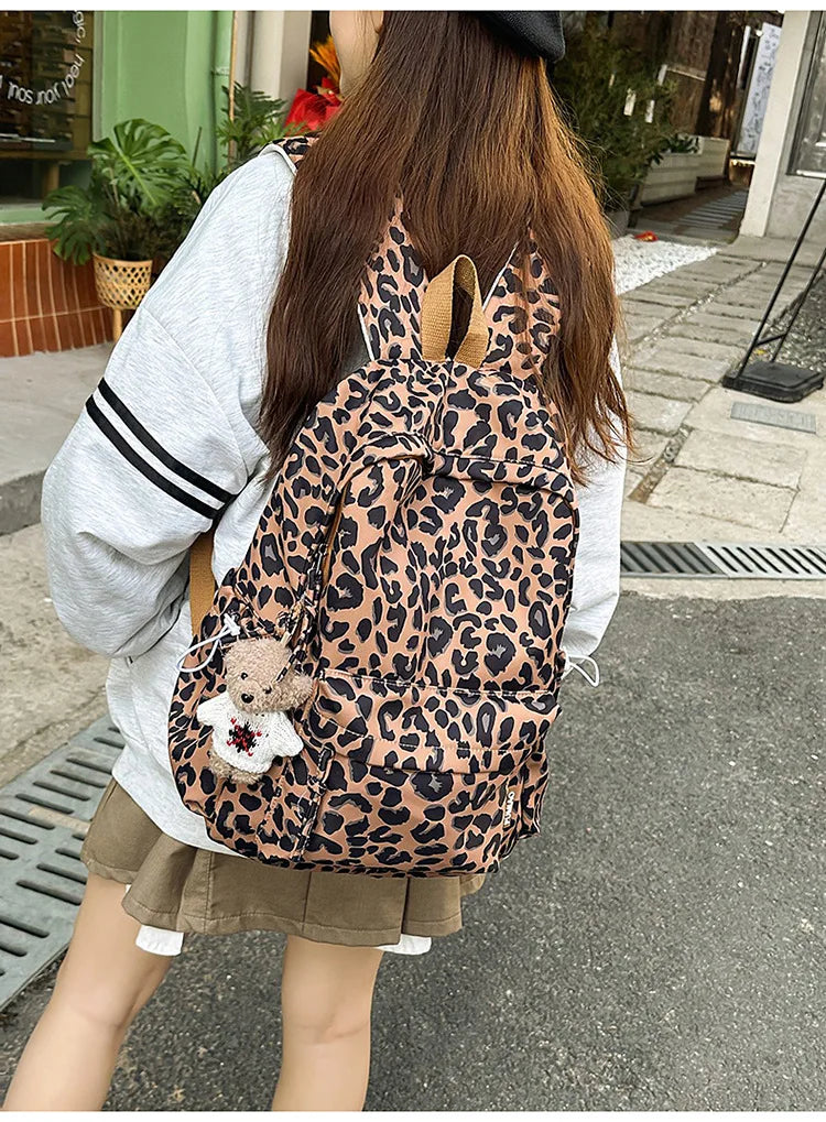 A woman is wearing a leopard print nylon backpack with multiple pockets while standing outdoors.