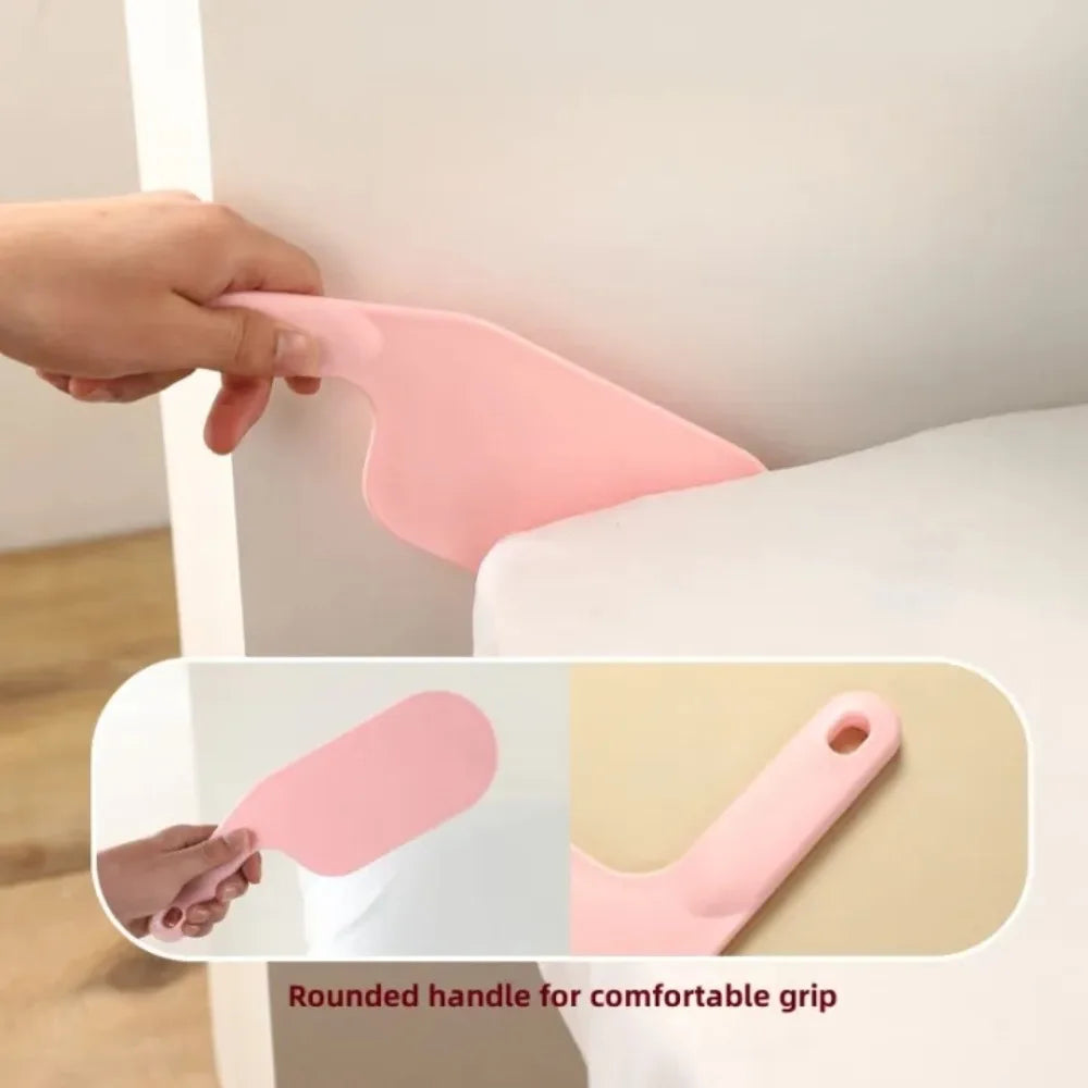 A hand is shown using a pink rounded handle bed sheet tucking tool on a white surface.