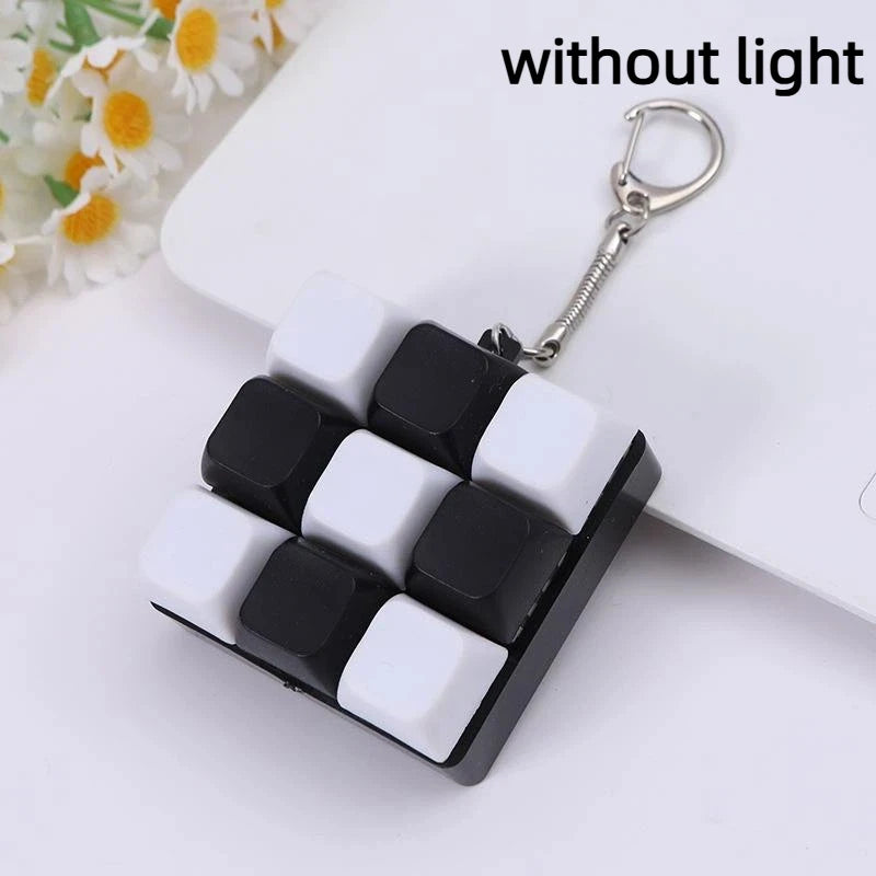A black and white mechanical keychain fidget toy with custom keycaps is shown against a white background.