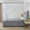 A full bed draped with a sheer white lace canopy mosquito net in a bright room.