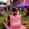 A pink laundry bag is placed on a pink mat on the grass in front of a concert stage.