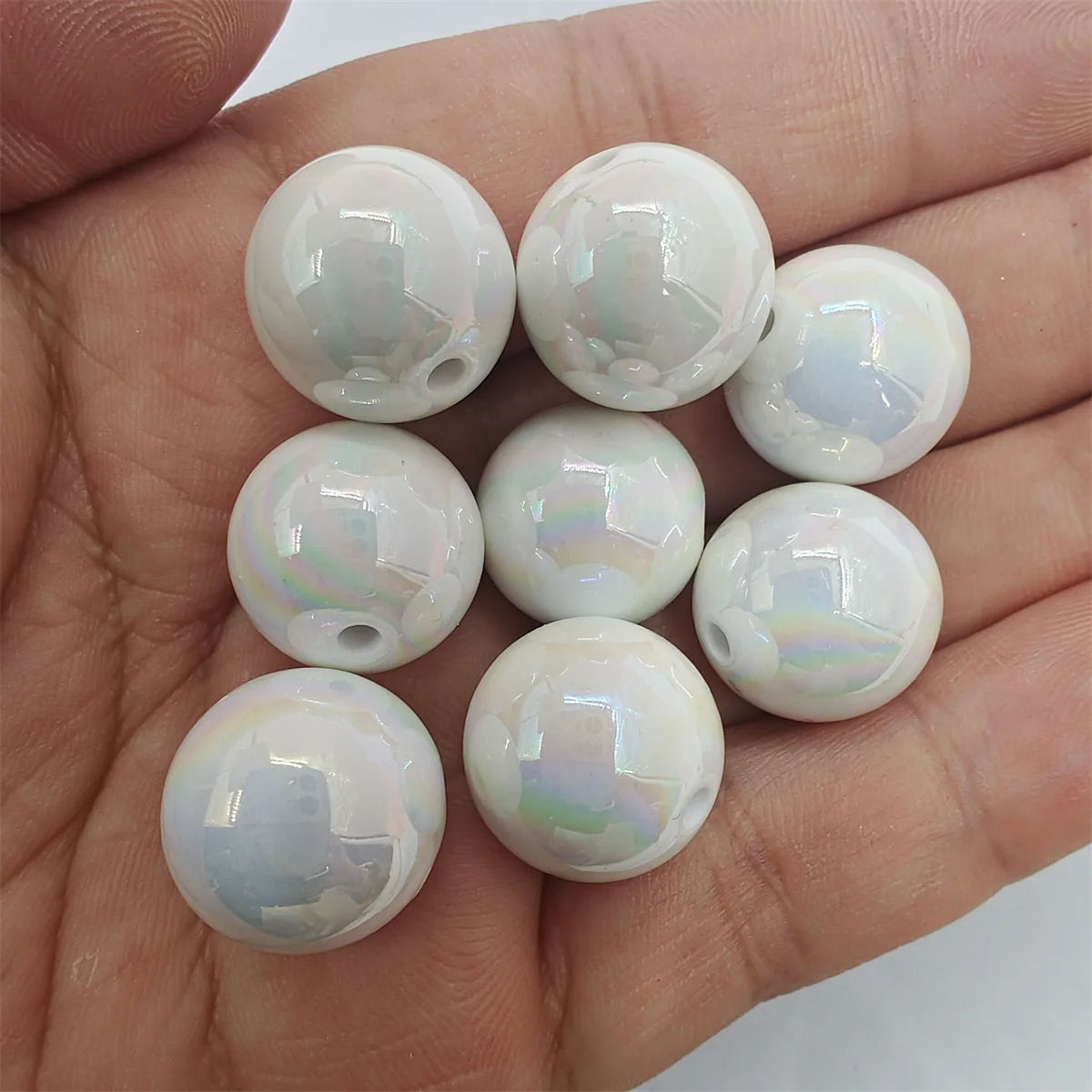 A hand holds several round, iridescent white acrylic beads for jewelry making.