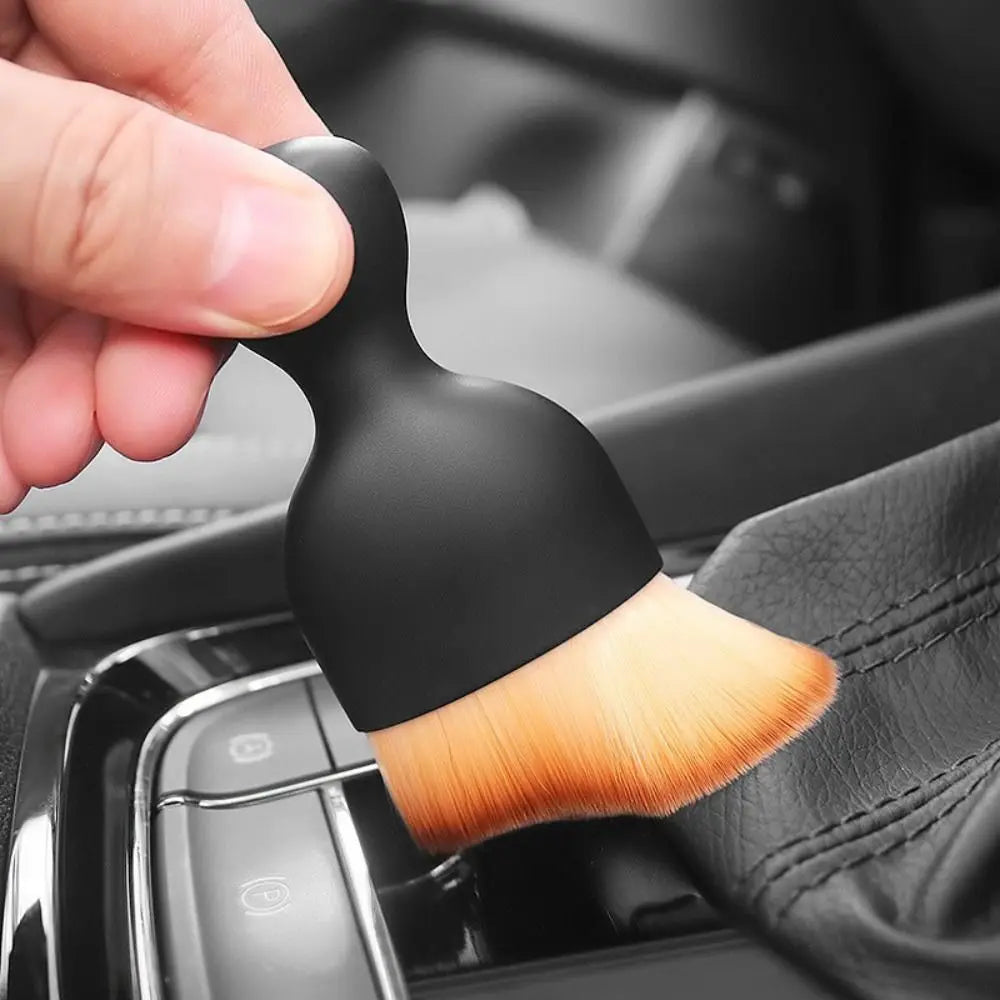 A hand holds a black ultra-soft curved detailing brush, used for cleaning car vents and gaps.
