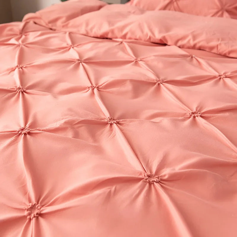 A close-up of a pink satin pinch pleated duvet cover set with quilted texture.