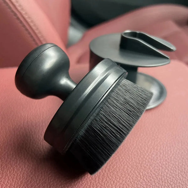 A black ergonomic tire shine applicator brush with a storage case rests on a pink surface.