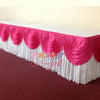 A long table skirt in white and pink fabric with ruffled draping displayed on a red carpet.