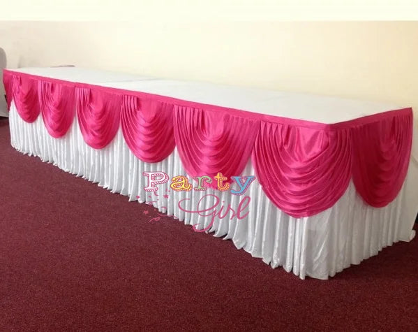 A long table skirt in white and pink fabric with ruffled draping displayed on a red carpet.