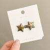A gold-toned star-shaped metal brooch or belt buckle is displayed on a white product tag.