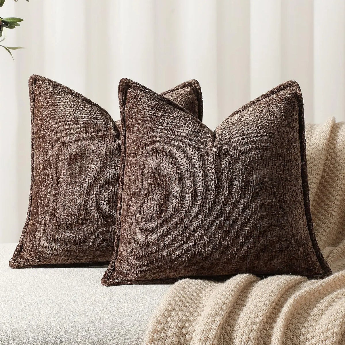 A dark brown textured chenille decorative cushion cover square throw pillow resting on a cream knitted blanket.