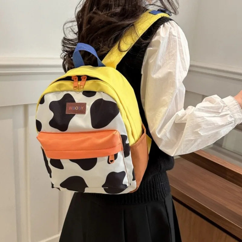 A yellow backpack with a cow print pattern and an orange accent pocket worn by a person.