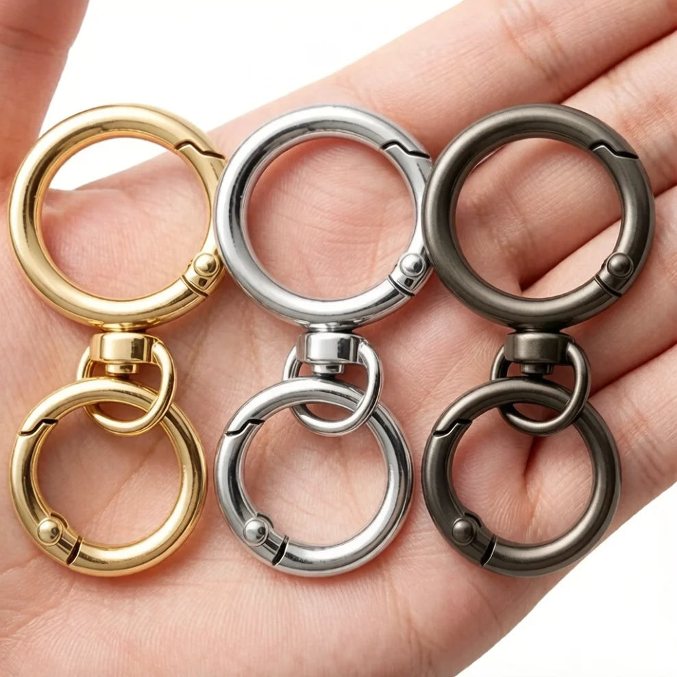 Three round spring snap hooks in gold and silver metal alloy carabiners held in a hand